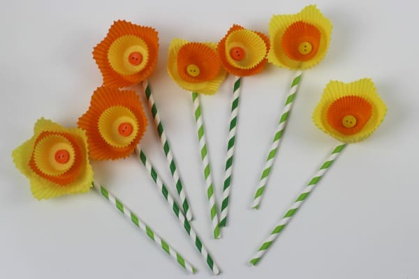 A number of yellow and orange cake cases layered to look like daffodil flowers with buttons in the center and paper straws as stems