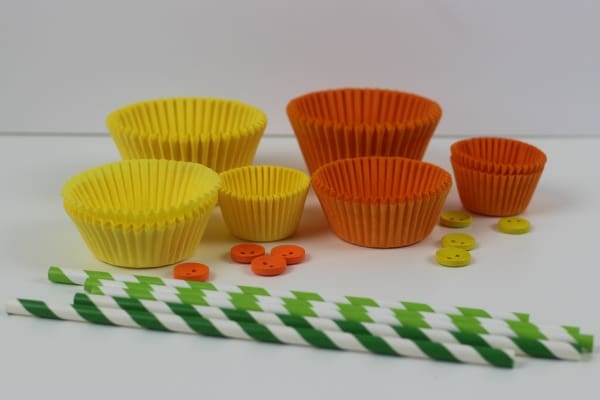 A selection of yellow and orange cake and bun cases, yellow and orange buttons and green striped paper straws to make cake case daffodils