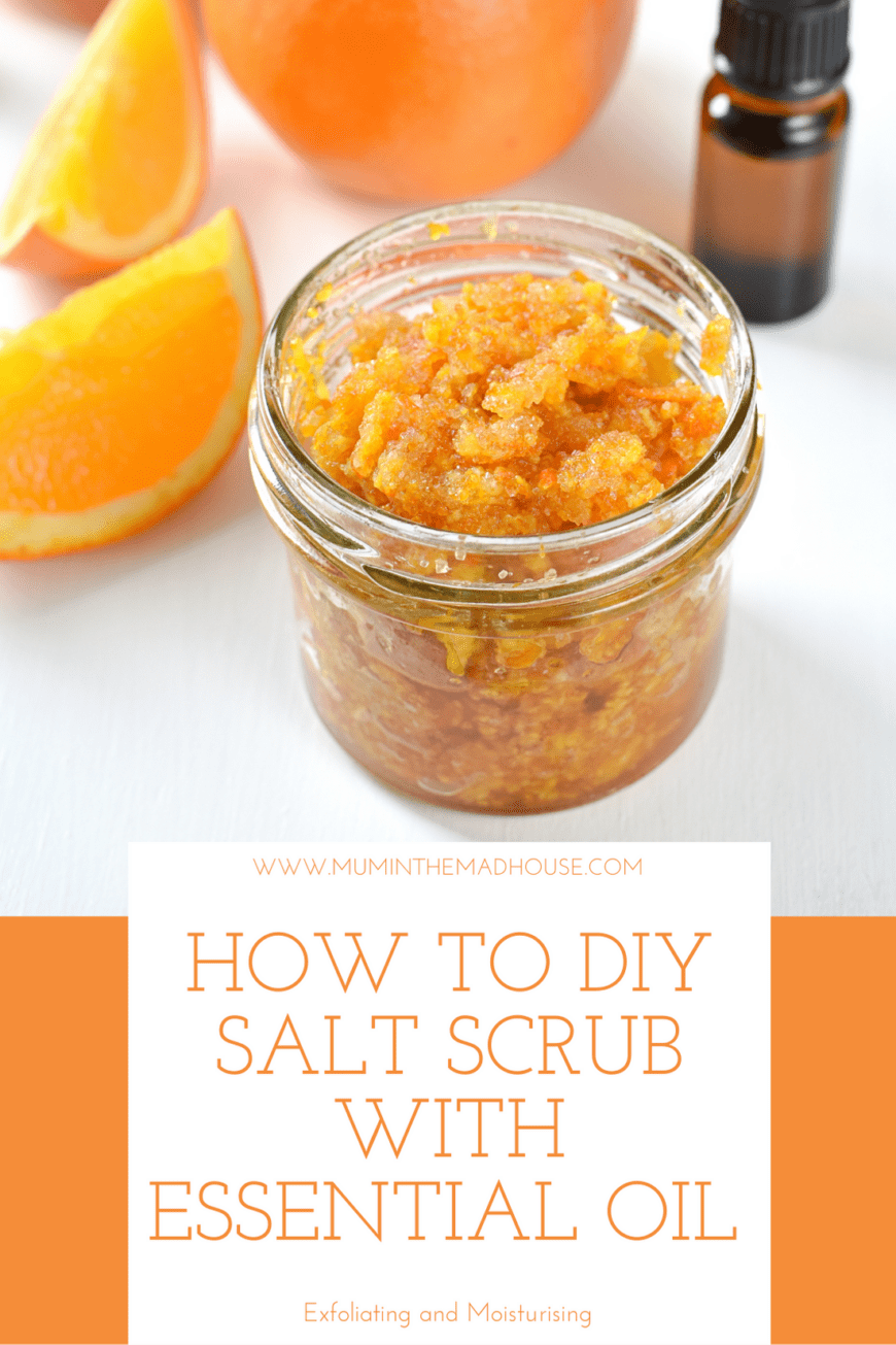 A jar of homemade salt scrub with a bottle of essential oil in the background and orange segments