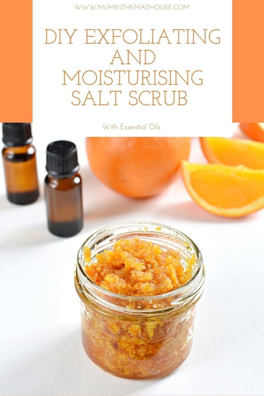 A jar of homemade salt scrub with two bottles of essential oil in the background and orange segments