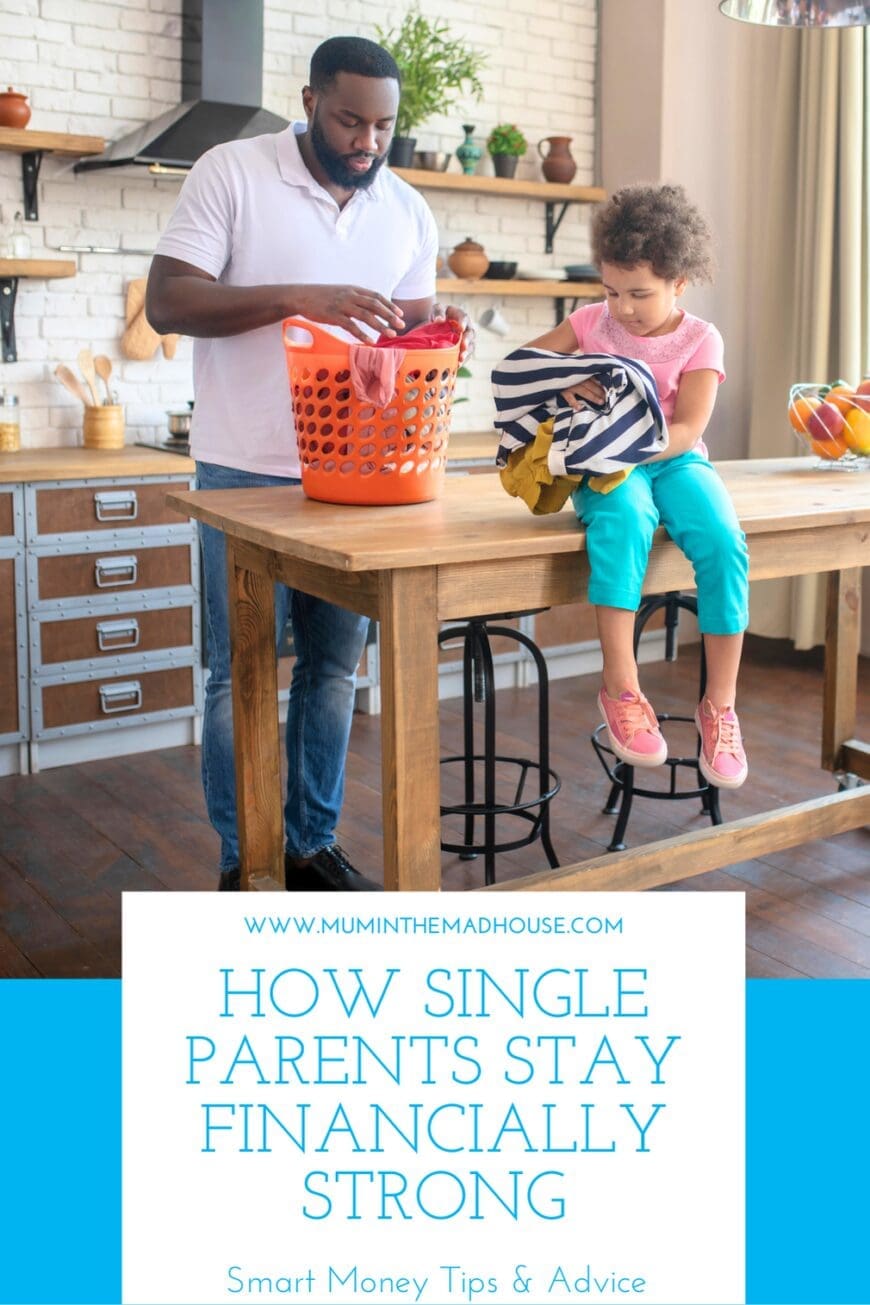 A father and his daughter in a rustic-style kitchen. The father is sorting laundry into an orange basket while the child sits on the table holding clothes. The text overlay reads ‘How Single Parents Stay Financially Strong – Smart Money Tips & Advice’ with the website Mum in the Mad House.
